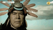 a man wearing a native american headdress with feathers on it is looking at the camera .