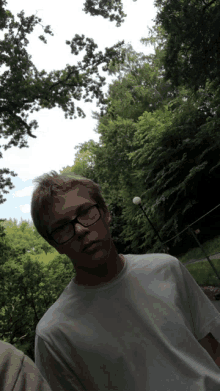 a man wearing glasses and a white shirt stands in front of a forest