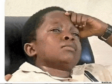 a young boy is laying in a chair with his hand on his forehead .