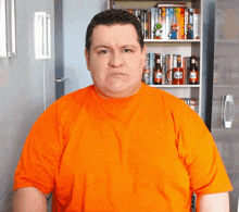 a man in an orange shirt is standing in front of a shelf full of books and bottles of beer