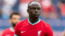 a soccer player is wearing a red shirt and looking at the camera during a game .