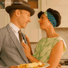 a man in a suit and tie holds a plate of food and a woman in a green dress looks at him