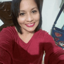 a woman in a red shirt is taking a selfie and smiling for the camera .