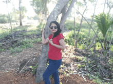 a woman wearing sunglasses leans against a tree in the woods