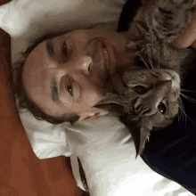 a man is laying on a pillow with a cat on his chest