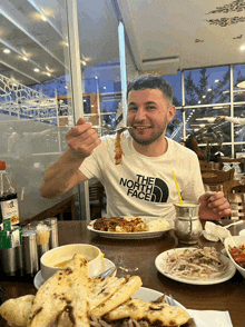 a man wearing a white north face t-shirt is eating food