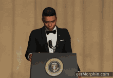 a man in a tuxedo stands behind a podium with the seal of the president of the united states of america