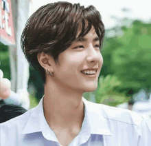 a young man wearing hoop earrings and a white shirt is smiling