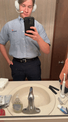 a man wearing headphones takes a picture of himself in a bathroom mirror