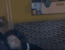 a man laying on a leopard print couch with a mask on the wall behind him