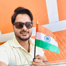 a man wearing sunglasses holds a small indian flag in his hand