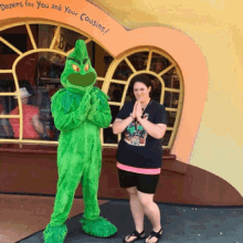 a woman stands next to a grinch mascot in front of a store that says dozens for you and your cousins