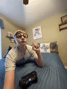 a boy wearing glasses is laying on a bed with a controller