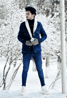 a man in a blue jacket stands in the snow holding a bottle