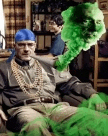 a man with a bandana on his head is sitting on a couch with a green smoke coming out of his mouth