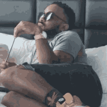 a man with a beard is sitting on a bed wearing sunglasses and a watch .