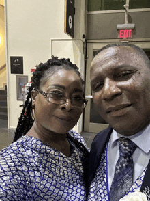 a man and a woman pose for a photo in front of an exit sign