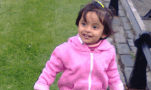 a little girl in a pink jacket is smiling and looking at the camera