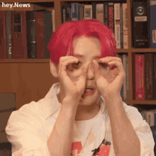 a man with red hair is covering his eyes with his hands while sitting in front of a bookshelf .