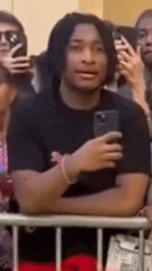 a man in a black shirt is holding a cell phone while standing in a crowd .