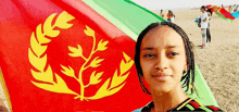 a woman stands in front of a red green and yellow flag with a laurel wreath on it