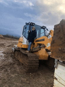 a woman leans against a liebherr bulldozer in a muddy field