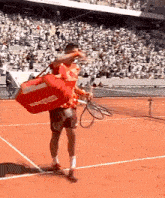 a man is holding a tennis racquet on a tennis court while carrying a red bag that says babolat on it