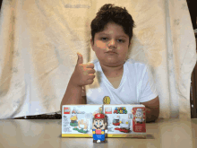 a young boy giving a thumbs up next to a box of super mario