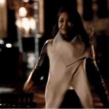 a woman in a white and black jacket is walking down a street at night .