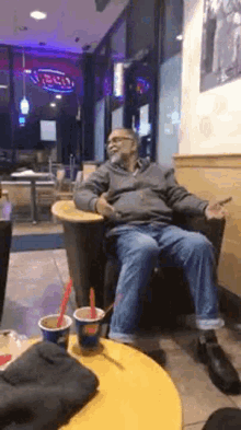 a man is sitting in a chair in a restaurant with a cup of ice cream in front of him .