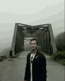 a man stands in front of a bridge with a foggy sky behind him