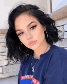 a woman wearing hoop earrings and a blue shirt with the word my on it