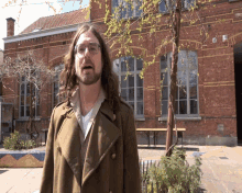 a man with long hair and glasses stands in front of a brick building with a sign on it that says ' a '