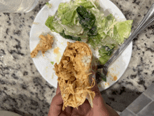 a person is holding a piece of food in front of a plate of salad