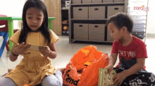 a boy in a red shirt with the word win on it sits next to a girl holding a cell phone