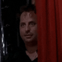 a man is peeking through a red curtain .