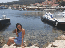 a woman sits on a rock near a body of water with boats in the background including a yamaha boat