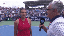 a woman in a red nike shirt is being interviewed by a man with a microphone on a tennis court