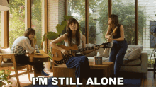 a woman playing a guitar in a living room with the words " i 'm still alone " below her