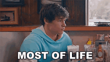 a young man is sitting at a table in a diner with the words most of life written above him .