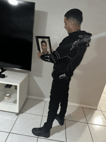 a man in a black jacket is holding a framed picture of a man with the name chris on it