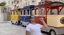 a man wearing sunglasses is sitting in front of a toy train that says ' trolley ' on the side