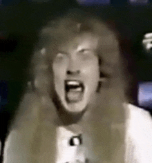 a man with long hair is screaming with his mouth open in a video .