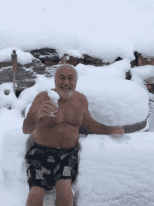 a man in shorts is sitting in the snow holding a glass of wine