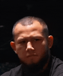 a man with a beard and a black shirt is looking at the camera with a serious look on his face .