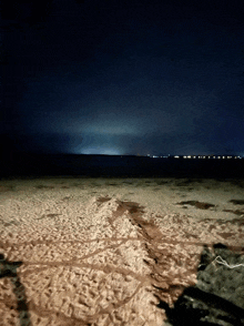 a beach at night with a dark sky and a few lights in the distance