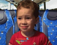 a young boy in a red shirt is sitting in a bus with blue seats .