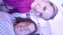 a woman in a hospital gown smiles next to another woman in glasses