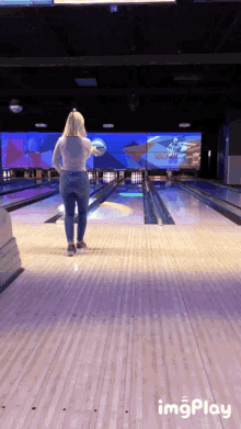 a woman throws a bowling ball at a bowling alley with a screen behind her that says imgplay on it