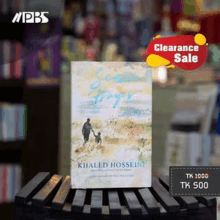 a book by khaled hosseini is sitting on a wooden shelf .